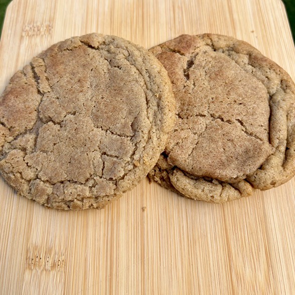 Two Chai Spice Brown Sugar cookies with crackled tops on a wooden board