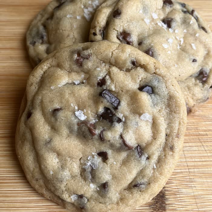 Chocolate chip cookies with dark chocolate chunks and flaky salt on a wooden board
